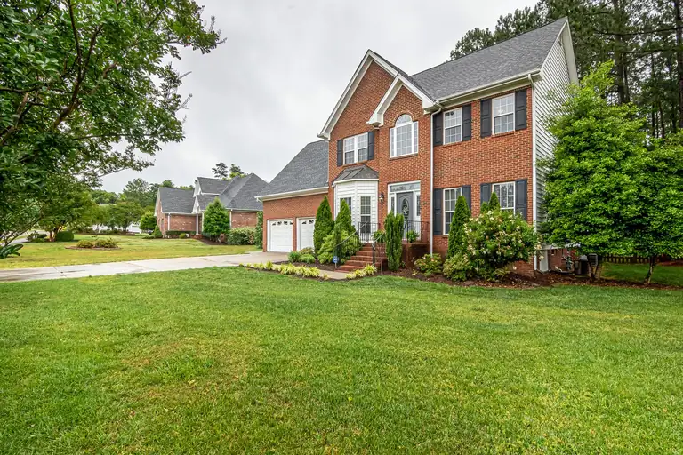 A two-storey brick home with a manicured front lawn and mature trees